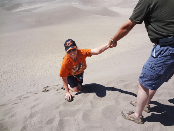A gentleman helps Karen climb up the soft sand dune.