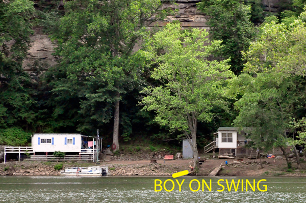 a boy on a swing by the cabins across the river